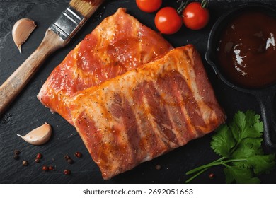 Ready for BBQ raw pork spare ribs with barbecue sauce. Black background. Top view.