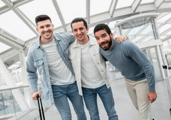 Ready For Boarding. Tourists Men Trio Hugging Posing With Luggage In Modern Airport Lounge. Guys Traveling Enjoying Vacation With Friends And Waiting For Their Flight. Travel Tickets Offer
