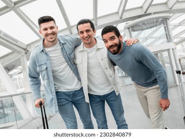 Ready for Boarding. Tourists Men Trio Hugging Posing With Luggage In Modern Airport Lounge. Guys Traveling Enjoying Vacation With Friends And Waiting For Their Flight. Travel Tickets Offer