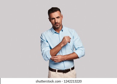 Ready to do things. Handsome young man adjusting sleeve and looking at camera while standing against grey background