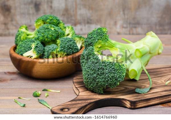 Ready to eat fresh uncooked broccoli on a\
cutting board and divided into inflorescences in a wooden plate\
behind on a wooden table. Healthy lifestyle, nutrition and zero\
waste concept. Close-up