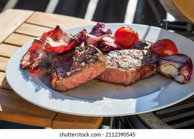 ready to eat - a grilled steak with onions, paprika and cherry tomatoes on a white plate on the balcony at a cold sunny winter day