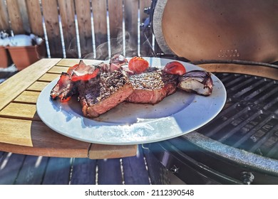 ready to eat - a grilled steak with onions, paprika and cherry tomatoes on a white plate on the balcony at a cold sunny winter day