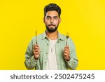 Ready to eat. Hungry Indian man waiting for serving dinner dishes with with restlessness holding cutlery fork knife will appreciate delicious restaurant meal. Excited guy isolated on yellow background