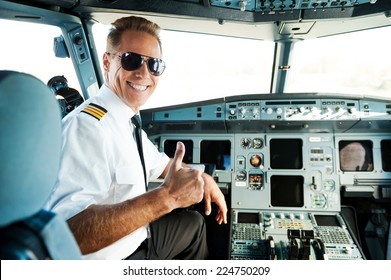 Ready to flight. Rear view of confident male pilot showing his thumb up and smiling while sitting in cockpit 