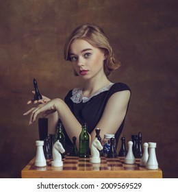 Ready For Game. Young Woman In Art Action Isolated On Brown Background. Retro Style, Comparison Of Eras Concept. Beautiful Female Model Like Legendary Chess Player, Queen Or Duchess, Old-fashioned.