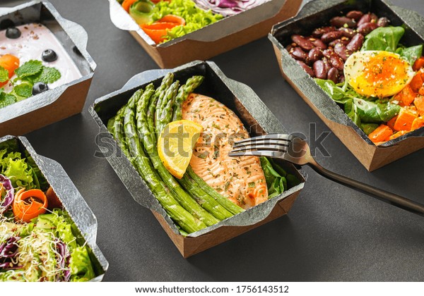 Ready healthy food catering menu in lunch boxes\
fish and vegetable packages as daily meal diet plan courier\
delivery with fork isolated on black table background. Take away\
containers order concept.