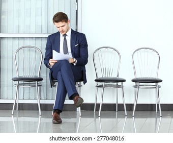 Ready for interview. Thoughtful man in formalwear holding paper while sitting at the chair in waiting room