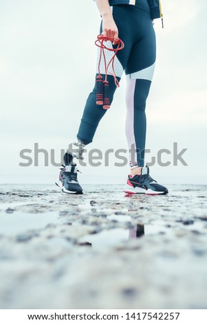 Ready to jump. Cropped image of young woman with prosthetic legin sports clothing holding skipping rope while standing in front of the sea