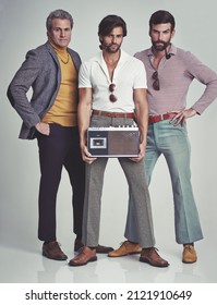 Ready to kick it retro style. A studio shot of three men clad in retro 70s wear holding a cassette player.