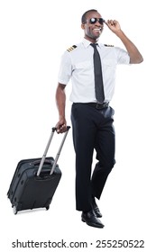 Ready To New Flight. Happy African Pilot In Uniform Walking And Carrying Suitcase While Being Isolated On White Background