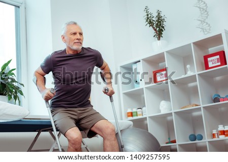 I am ready. Nice elderly man holding crutches while preparing to get up