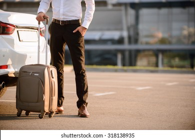 Ready for official journey. Pleasant confident businessman standing near his car and holding suitcase while going to travel