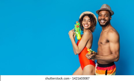 Ready For Pool Party. Happy Black Couple Holding Water Guns, Blue Studio Background, Empty Space