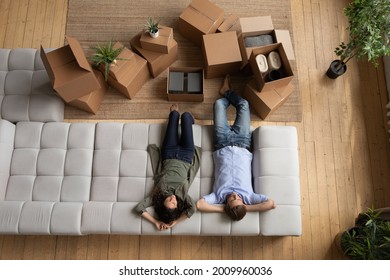 Ready to relocate. Top view of loving young married couple sit relax on cozy couch after packing stuff. Happy spouses resting on sofa waiting for transportation service to move things to new dwelling - Shutterstock ID 2009960036