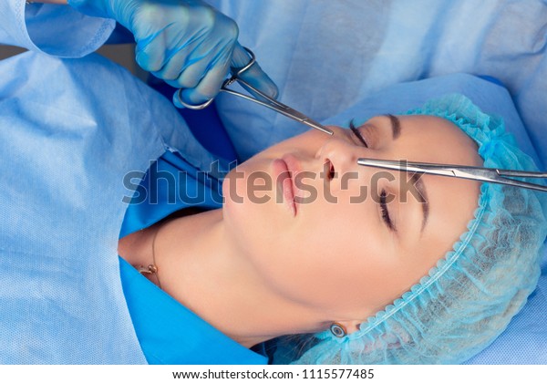 Ready for rhinoplasty. People, cosmetology,\
plastic surgery and beauty concept - surgeon or beautician hands\
touching woman nose with medical tools instruments preparing for\
nose job in medical\
clinic