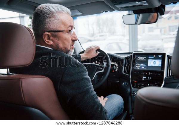 Ready to the ride. View\
from behind of senior businessman in official clothes driving a\
modern new car.