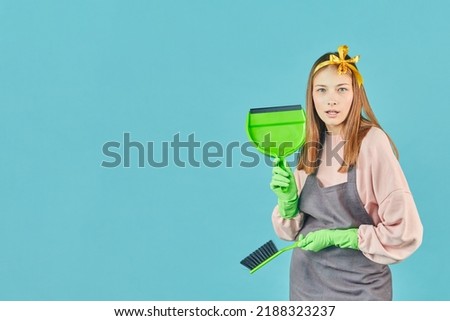 Ready For Spring-Cleaning. Portrait of joyful girl with household supplies in hands over blue background. Young woman hold dustpan and brush.