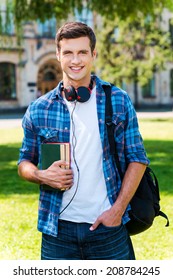 Ready to study. Handsome young man holding books and smiling while standing in front of his university