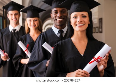 Ready To Success. Four College Graduates Standing In A Row And Smiling