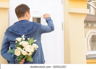 Ready For Surprise. Nice Cheerful Upbeat Young Guy Holding Bouquet Of Flowers And Standing Near The Door While Knocking