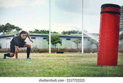 Ready to tackle the bag. Full length shot of a handsome young rugby player working out with a tackle bag on the playing field. - Powered by Shutterstock