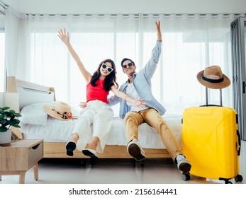 Ready to travel, happy holiday, check-in. Summer vacation concept. Asian couple raising hands with joy, man and woman wear sunglasses smile with happy on white bed with yellow suitcases on a trip.