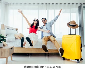 Ready to travel, happy holiday, check-in. Summer vacation concept. Asian couple raising hands with joy, man and woman wear sunglasses smile with happy on white bed with yellow suitcases on a trip. - Shutterstock ID 2161587883
