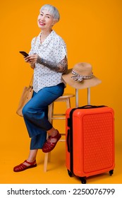 ready to travel ,old senior asian smiling cheerful female woman hand using smartphone online booking pull luggage bag prepare to new abroad journey travel studio shot on yellow background - Shutterstock ID 2250076799