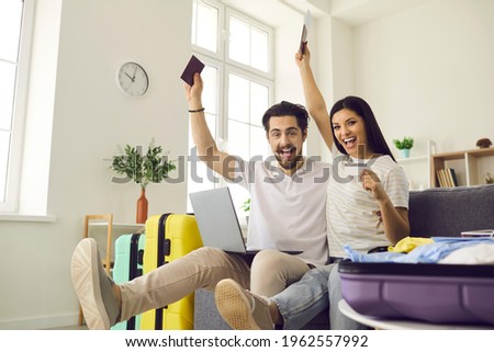 Ready for vacation. Happy young couple in love having fun on couch at home glad they've packed travel bags, picked airline online and bought tickets that soon will get them to trip destination abroad