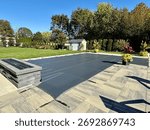 Ready for winter in fall. Custom winterized J-shaped built-in, inground pool with safety Loop - Loc mesh cover to protect. Melting snow, rain drains through. Brass anchors are flush to paver height.  