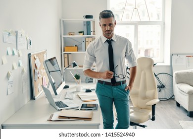 Ready to work. Good looking young man looking at camera and smiling while standing in the office