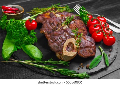 Ready-cooked beef meat Osso buco Veal shank on black stone board. Ingredients for Osso buco thyme, parsley, rosemary, lettuce, pepper, sage. Dark wooden background - Powered by Shutterstock