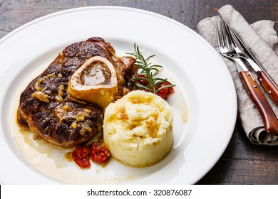 Ready-cooked Osso buco Veal shank with tomatoes and mashed potatoes on white plate on wooden background