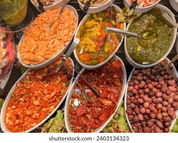 Ready-made food in trays, seasoned olives, sun-dried tomatoes in oil and bell pepper salad with olive oil, anchovies with green sauce and shrimp with Aurora sauce, displayed for sale on deli counter  - Powered by Shutterstock