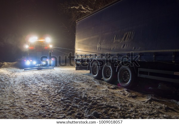 A real accident. Truck traffic accident at\
night, on a snowy winter road.\
Strongly illuminated Wrecker truck\
pulls a truck out of snow\
hanging.
