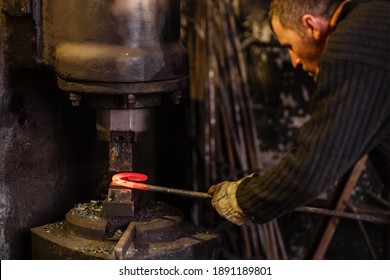 Real brutal blacksmith works in a workshop mechanical hammer with a red-hot iron. Portrait of a profession.