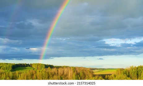 A real double rainbow in a cloudy sky after heavy rain. A rare natural phenomenon in the blue sky. Rainbow over hilly countryside in early spring. The concept of weather forecast and climate change.