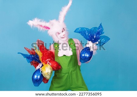 Real easter bunny with lots of chocolate eggs on colorful background with free space for text