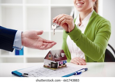 Real estate agency. Woman broker offering key of new house to male client. 
