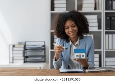 Real estate agent, American businesswoman African pointing to house model explaining house plan to client in office deal. Concept. Mortgage, mortgage, insurance, rent, house sale. - Shutterstock ID 2311591055