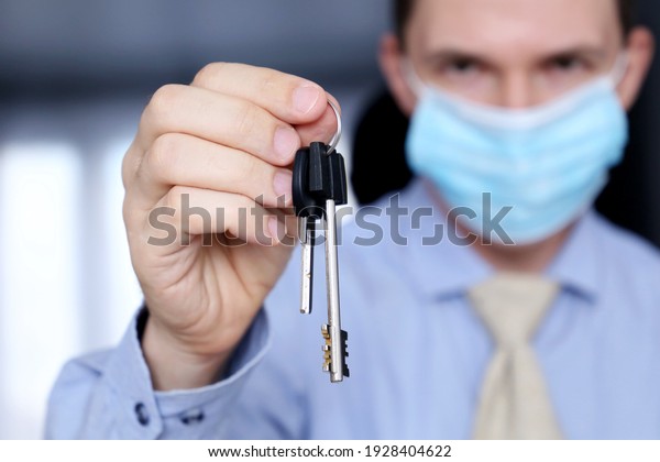 Real estate agent, apartment keys in\
male hands. Man in medical face mask and office clothes, concept of\
purchase or rental home during coronavirus\
pandemic
