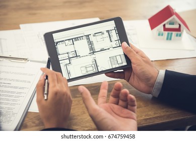 Real estate agent with client or architect team discussing house floor plan on tablet computer screen - Powered by Shutterstock