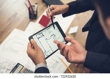 Real estate agent with client or architect team discussing a housing model and its blueprints digitally using a tablet computer - Powered by Shutterstock