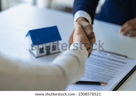 Real estate agent and client handshake after completion contract after home insurance to start project contract in office center at construction site behind model house, home loan contract concept