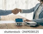 A real estate agent and a customer discuss a contract to buy insurance or a loan on real estate or property. A real estate agent shakes hands and delivers a sample home to the customer.