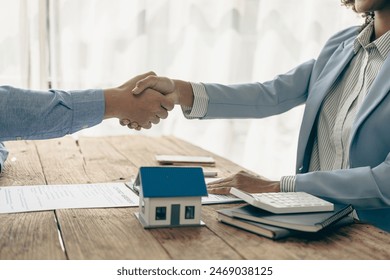 A real estate agent and a customer discuss a contract to buy insurance or a loan on real estate or property. A real estate agent shakes hands and delivers a sample home to the customer. - Powered by Shutterstock