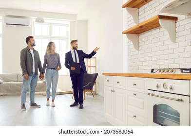 Real Estate Agent Giving Clients Tour About All Rooms In Big New House. Married Couple Planning To Buy New Home, Meeting With Realtor And Looking At Light Spacious Studio Apartment With White Walls