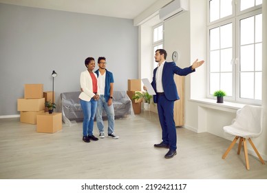 Real Estate Agent Giving House Tour To Future Tenants Or Potential Buyers. Boyfriend And Girlfriend Or Husband And Wife Planning To Buy New Home And Meeting With Realtor In Modern, Big, Spacious