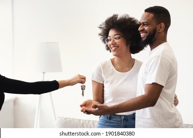 Real Estate Agent Giving New House Key To Happy Black Couple After Buying Apartment Standing Indoors. New Home, Property Purchase, Mortgage And Ownership Concept